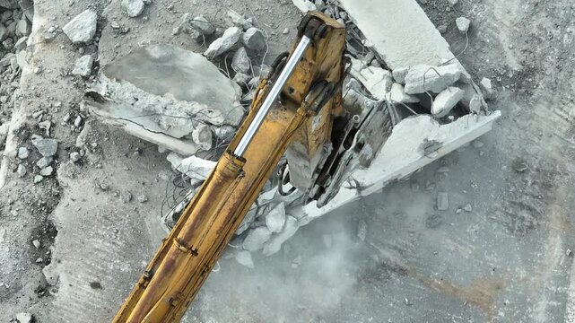 Aerial drone view of a hydraulic breaker demolishing a concrete road surface, generating rubble and dust during infrastructure renewal, urban redevelopment, and construction site operations. 4k.
