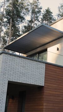 Vertical video. Close-up of slatted roof and glass balcony on modern house with pine trees.