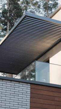 Vertical video. Modern house featuring a slatted roof and glass balcony with pine trees behind.