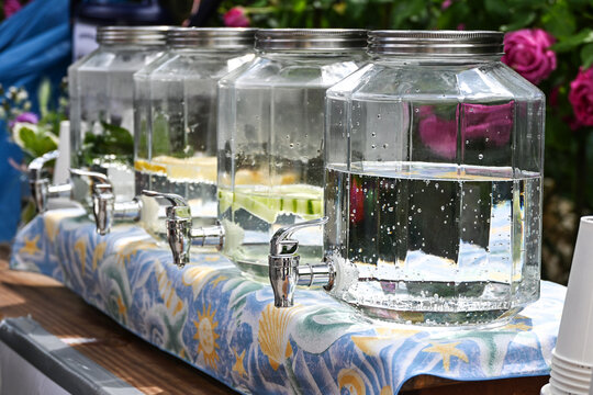 Large glass jar dispensers with tap faucets, filled with fresh water and some ingredients like lemon, cucumber or mint, to refresh visitors at a neighborhood street festival, copy space