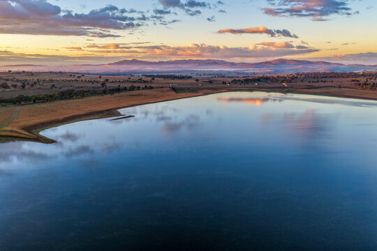 Aerial view at dawn over Lake Keepit featuring the dam wall, expansive reservoir and a foggy rural landscape beneath soft golden morning light in NSW, Australia.