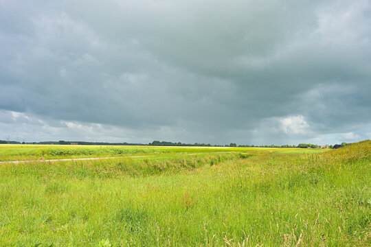 Vast green meadow and open landscape under a heavy, dramatic storm sky with dark, rolling clouds.