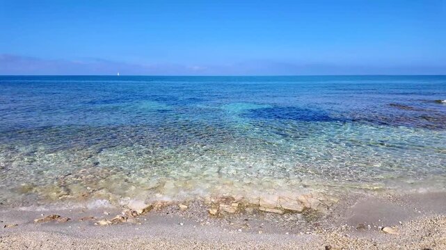 Crystal clear turquoise water and shallow rocky seabed at Is Arutas beach in Sardinia, Italy. Calm sea waves on a sunny summer day with a clear blue sky and horizon