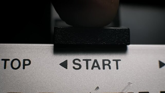 Macro view of a male finger pressing a textured black start button on a control panel. The extreme close-up highlights industrial design and machine activation concepts.