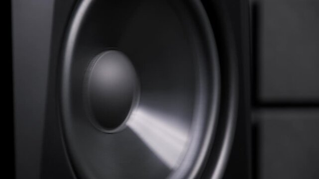 Close-up of a black subwoofer cone vibrating intensely from loud low-frequency bass. The dynamic membrane movement creates powerful sound waves in a dark studio setting.