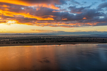 Fototapeta premium Aerial scene capturing a golden sunrise over Lake Keepit, with morning fog drifting across the surrounding rural landscape to create a peaceful and atmospheric setting in NSW, Australia.