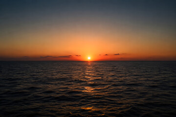 Fototapeta premium Beautiful sunset over calm ocean water with orange sky and clouds serene natural scene