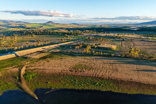 Aerial scene showcasing the Lake Keepit dam wall leading into the surrounding rural landscape, highlighting the expansive reservoir, engineering infrastructure and natural beauty in NSW, Australia.