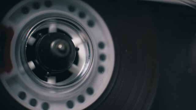 Macro top-down view of a single vintage audio cassette reel spinning. Transparent plastic and red markings are visible against a dark background in the tape player.