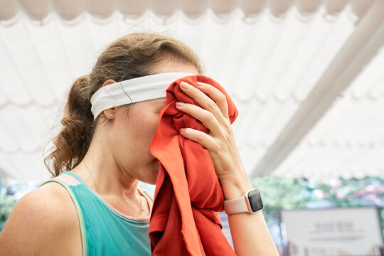 Close up of young woman covering her face with red towel, wiping sweat after pickleball match. Active sport lifestyle.