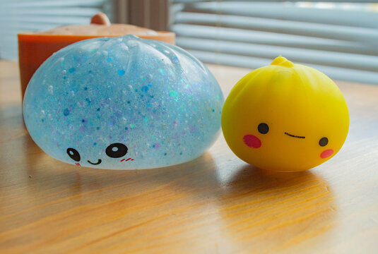 Cute blue dumpling shape squishy toy with a funny smiling face sitting on a plastic steamer box by the window.