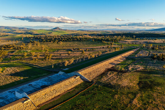 Aerial scene showcasing the Lake Keepit dam wall leading into the surrounding rural landscape, highlighting the expansive reservoir, engineering infrastructure and natural beauty in NSW, Australia.