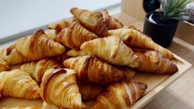 Golden croissants stacked on a wooden breakfast buffet tray, showing flaky layers, glossy crusts and a fresh hotel bakery spread.