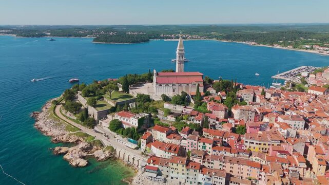 Drone flying toward Rovinj&rsquo;s old town and St. Euphemia church, revealing the peninsula, terracotta rooftops, and Adriatic coastline in bright summer light.