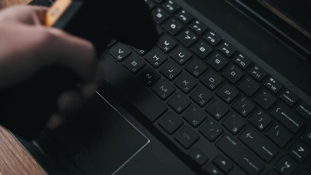 High-angle view of a hand using a rubber air blower to remove dust from a black laptop keyboard. This maintenance technique illustrates safe and effective computer hardware cleaning.
