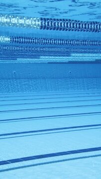Empty indoor swimming pool lane underwater view with blue reflections.
