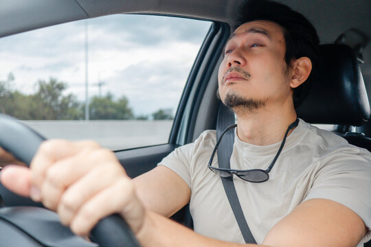 Tired Asian man feeling sleepy and exhausted while driving his car, battling fatigue on the road.