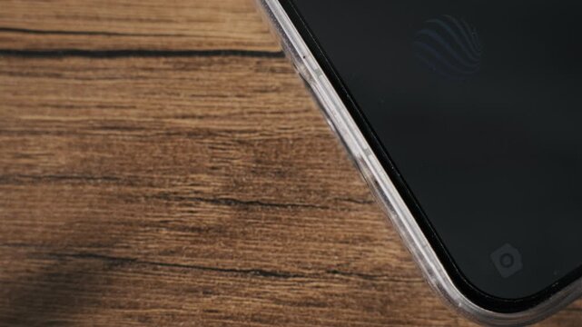 Macro view of fingers disconnecting a white USB-C cable from a smartphone charging port on a wood table. The transparent case and black screen emphasize modern mobile technology.