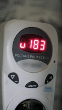 Vertical macro shot of a voltage protector red digital display showing fluctuating low voltage. The screen temporarily blacks out to indicate an unstable current.