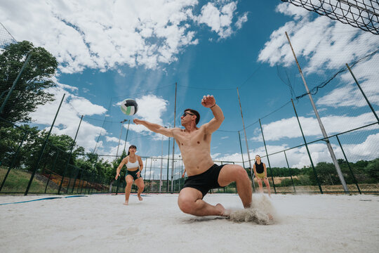 Three volleyball players dive and reach for the ball on a sandy outdoor court. Action shot shows teammates competing in a beach volleyball play under a blue sky.