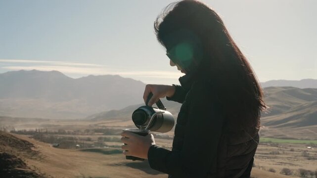 Medium Close-up of Woman Pouring Hot Water From Thermos Into Yerba Mate Gourd Against Andean Mountain Landscape