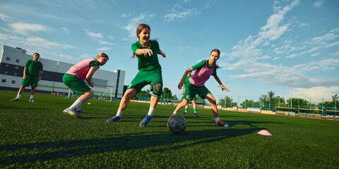 Obraz premium Girls soccer team dribbling ball during summer field practice. Concept of women football, match action, dribbling skills, teamwork, youth camp and sports advertising.