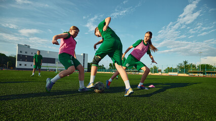 Naklejka premium Girls soccer players competing for ball during outdoor match drill. Concept of women football, teamwork, competitive action, dribbling skills, empowerment and summer tournament.