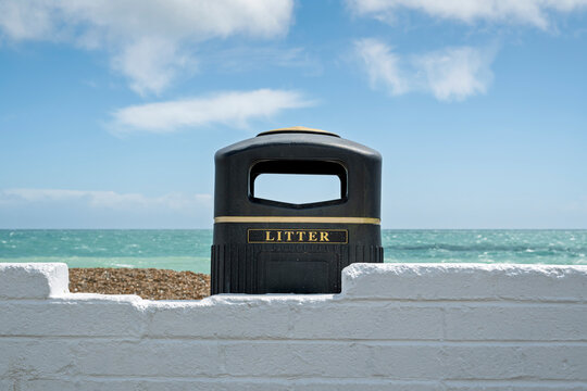 black litter bin by a white wall and beach