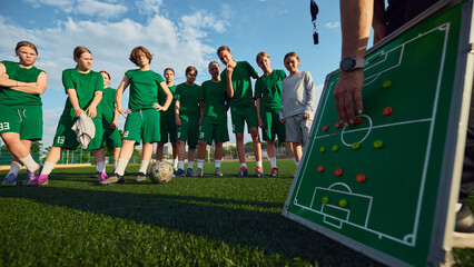 Girls soccer team listening to coach tactics on outdoor field. Concept of tactical coaching,...