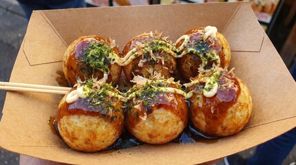 Obraz premium Freshly cooked Japanese takoyaki drizzled with savory sauces inside takeaway box, steaming street food