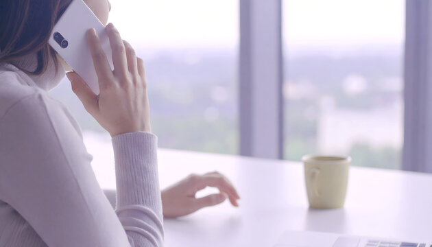 person, woman speaking on the phone while looking outside, white desk, coffee mug working, buissness