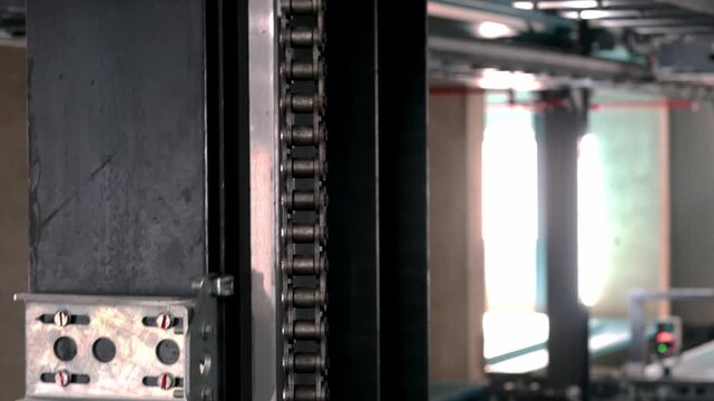 Close-up of a smart parking system mechanism with metal components, rollers, chain drive and safety mesh, showing automated garage technology used for modern vehicle parking operations.
