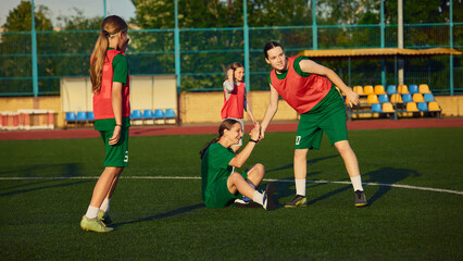 Obraz premium Teenage female soccer player helping teammate stand up after training fall. Concept of team culture, player support, youth football coaching, athlete wellbeing and positive sports environment.