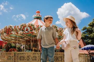 Obraz premium happy boy and girl on a carousel at an amusement park in the summer