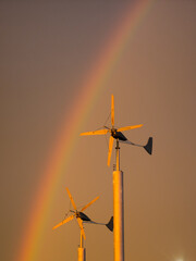 Fototapeta premium features two wind turbines silhouetted against a golden hour sky with a rainbow.