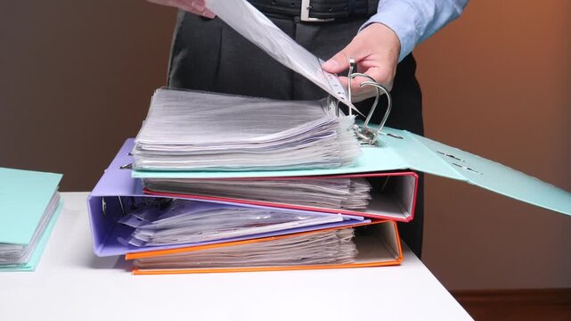 Employee hands sorting paperwork and filing important business records into colorful ring binders, representing administrative tasks and data archiving work
