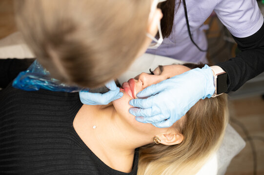 Top view of beautician applying permanent makeup on  woman lips. Cosmetic lip tattoo procedure in beauty salon. Professional artist working with covered micropigmentation machine. 