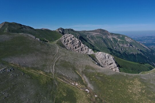 Aerial view of the rocky ridge of Palazzo Borghese in the Sibillini Mountains with grassy slopes and clear blue sky in Montemonaco, Marche, Italy.