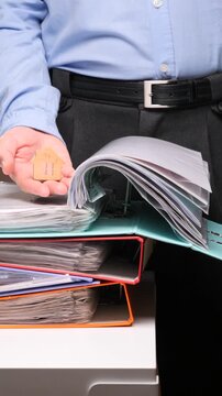 Vertical video person holding a small wooden house model over stacks of binders and files, symbolizing real estate transactions, property investment, mortgage documentation, or home ownership processe