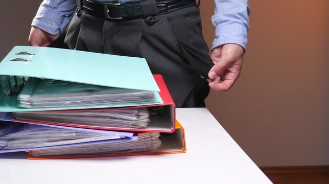 Man showing empty pockets beside towering binders of unpaid bills and paperwork, illustrating bankruptcy, debt, tax burden, unemployment and overwhelming financial crisis at work