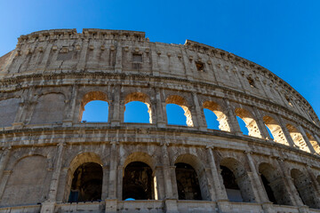 Naklejka premium Famous Coliseum in Rome. Colosseum, or Coliseum. Part of the wall of an antique stone structure with arches. Italy, Europe. Famous touristic place in the world, Europe. Beautiful blue sky background.
