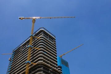 High-rise residential buildings under construction with yellow tower cranes against a blue sky. © jianjian