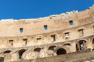 Fototapeta premium Famous Coliseum in Rome. Colosseum, or Coliseum. Part of the wall of an antique stone structure with arches. Italy, Europe. Famous touristic place in the world, Europe. Beautiful blue sky background.
