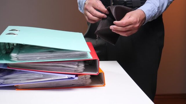 Person opening an empty wallet, demonstrating a financial crisis, debt, or personal bankruptcy, with stacked office binders representing overdue bills or business struggles