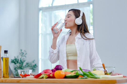 Asian women in good spirits hold glass clean water drink while cooking refresh themselves and ensure they have enough water which helps keep their bodies refreshed energetic beneficial health.