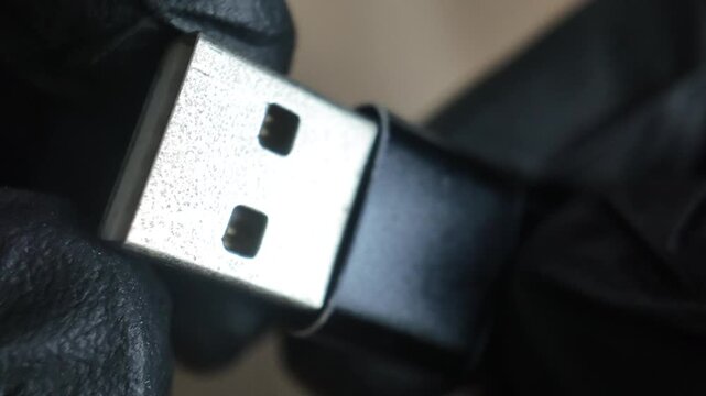 A detailed close up shot of a person in black gloves holding and rotating a sleek metal USB drive, showcasing the connector and compact memory storage design.
