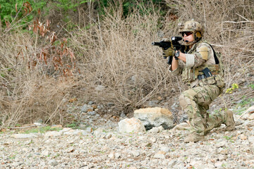 Fototapeta premium Soldiers prepare fire their guns at the enemy in front them ready attack stance : Soldiers wear camouflage uniforms in arid forest areas blend in with the wooded and mountainous terrain. 