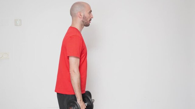 Side view of a man performing lateral shoulder exercises with dumbbells in the living room on a white background