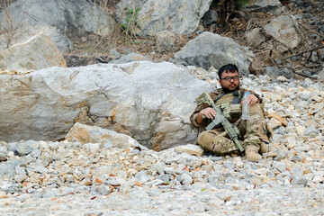 Fototapeta premium Soldier sat resting behind roc exhausted and covered in dust that had contaminated his uniform during training exercise.