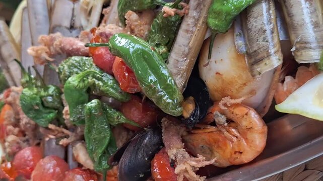Mixed seafood platter in metal tray &mdash; shrimp, crab claws, razor clams, fried squid, grilled peppers, cherry tomatoes, lemon, rustic restaurant style, extreme closeup video frames